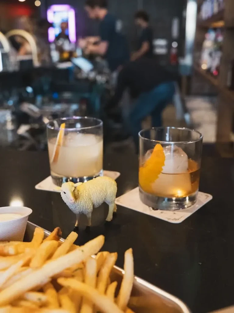 French fries, two cocktails, and a sheep figurine on a bar.