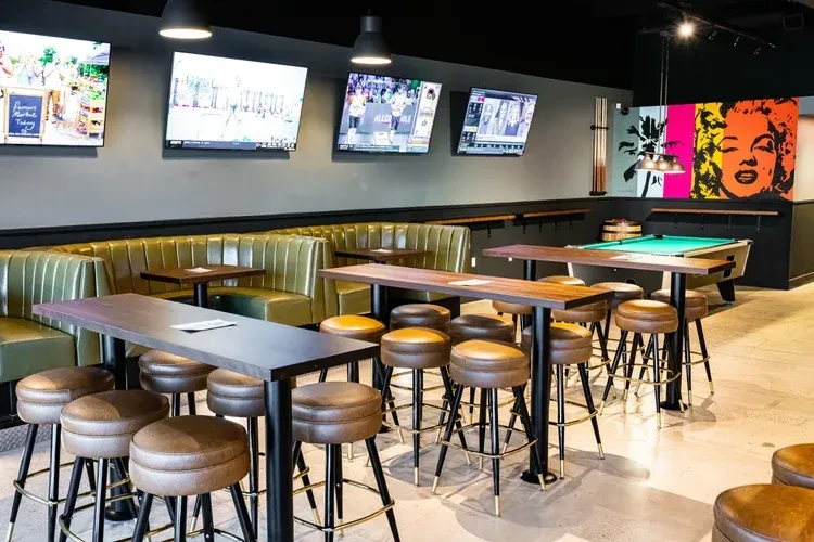Modern bar with booth, high-tops, sports TVs, pool table, pop-art mural.