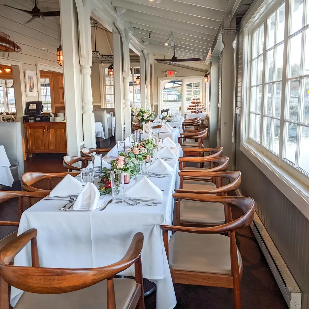 Elegant waterfront dining room with long banquet tables and floral decor.