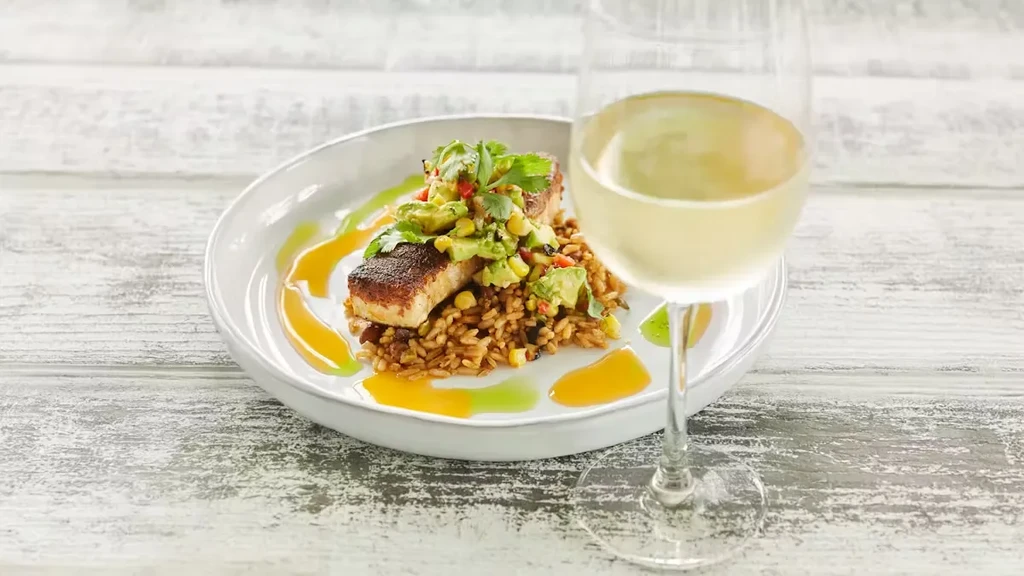 Professionally plated seared fish with avocado salsa, rice, and white wine.