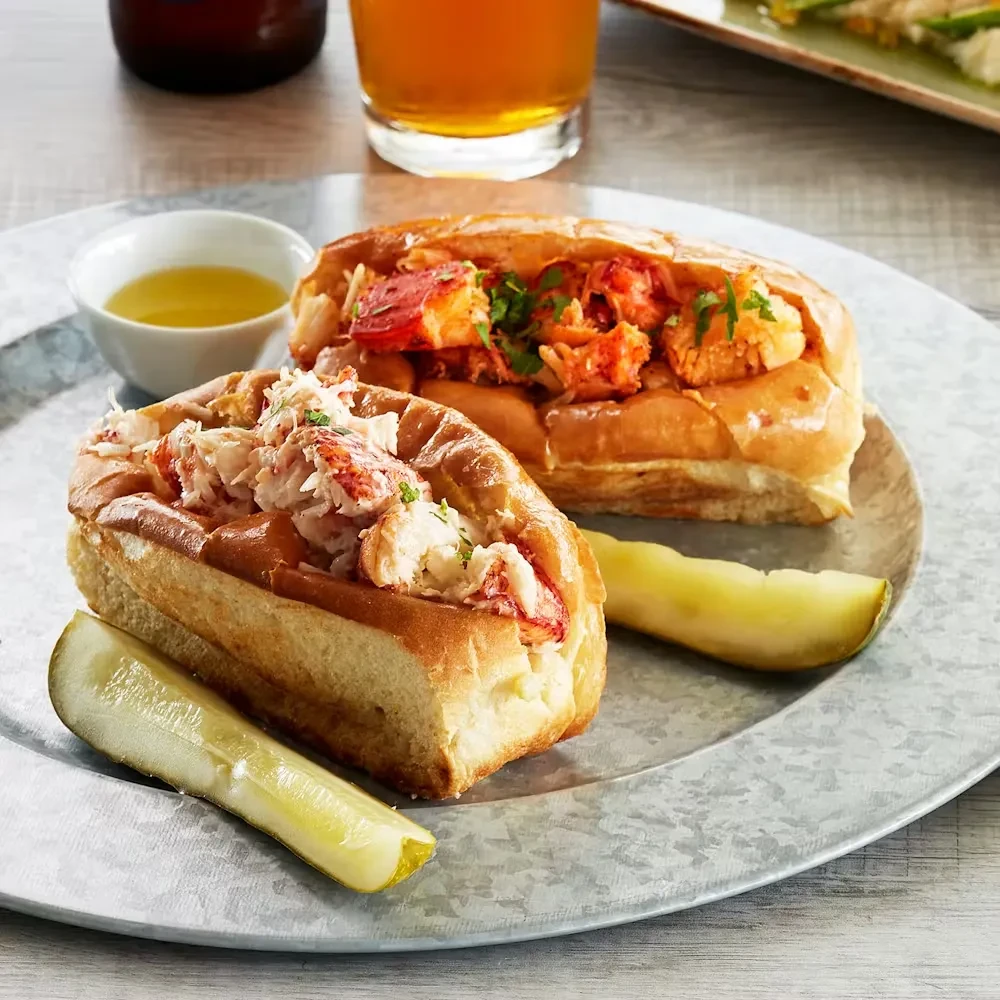 Cold and warm lobster rolls with pickle spears and melted butter.