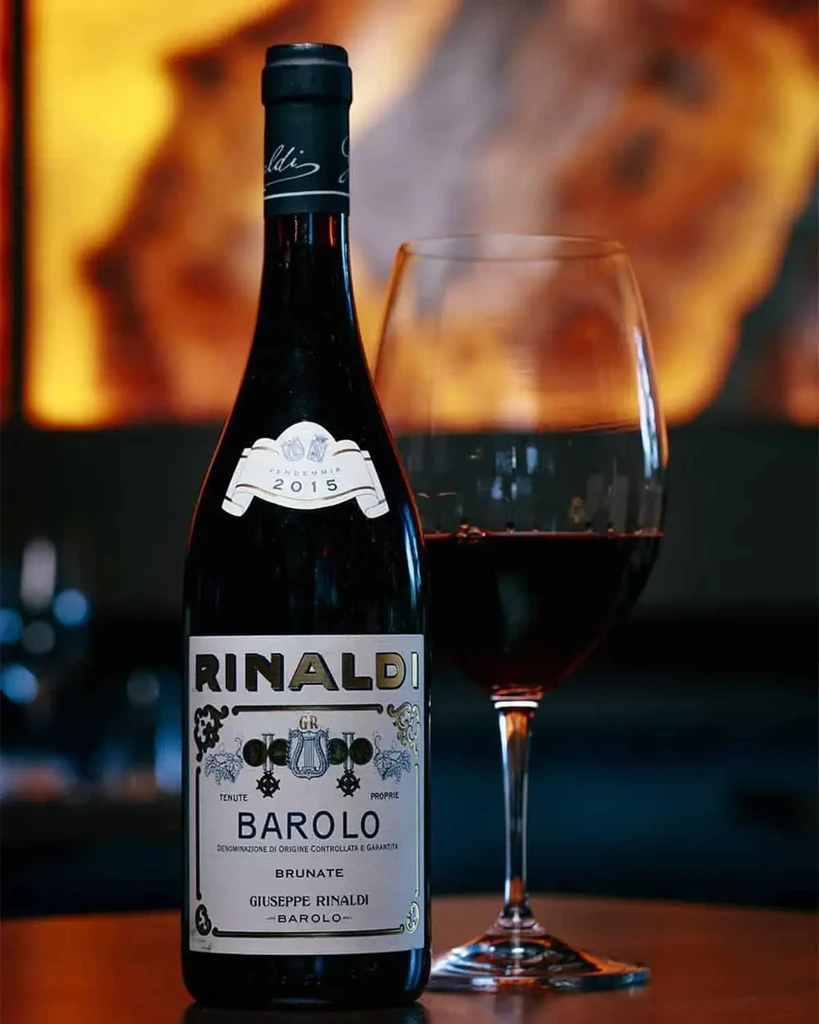 Dark RINALDI BAROLO BRUNATE 2015 wine bottle, blurred glass of red wine.