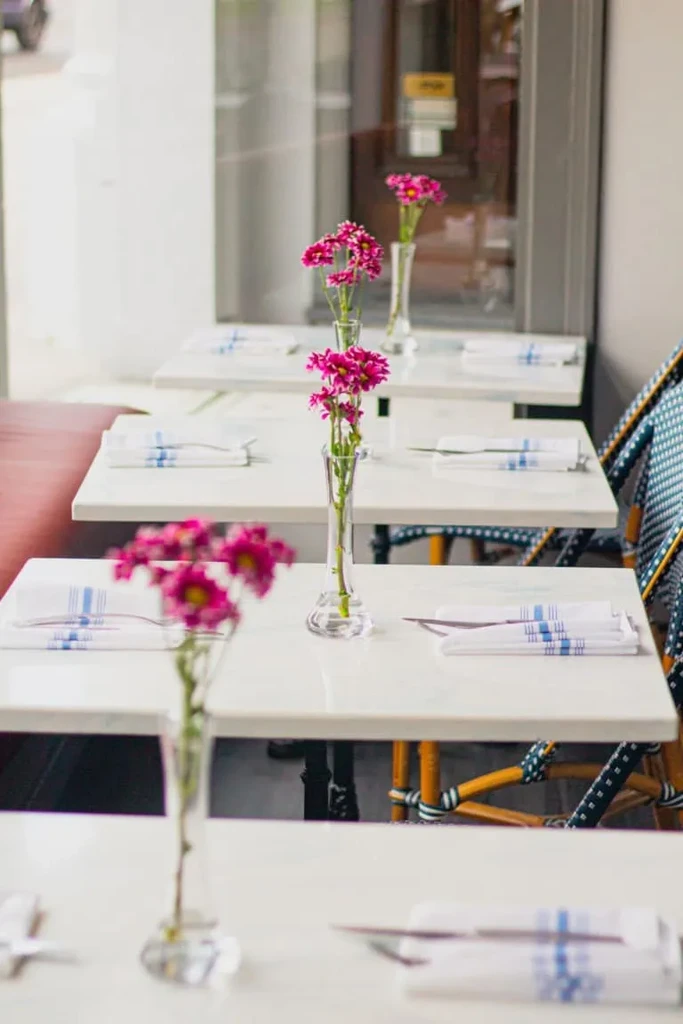 White restaurant tables with blue-striped napkins and fuchsia daisy flowers.