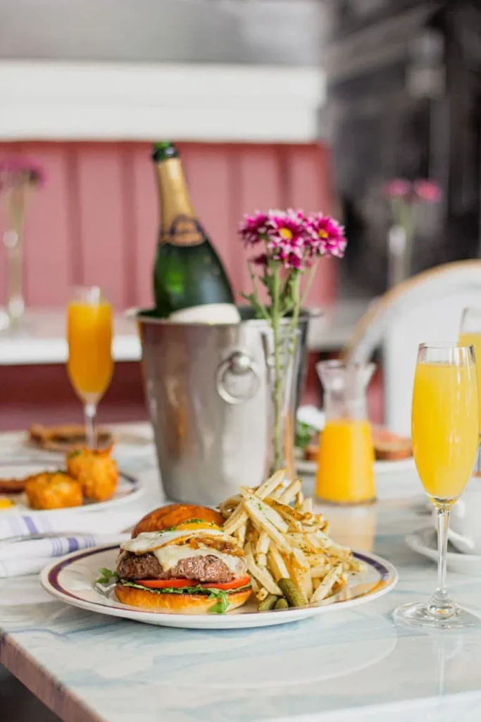 Gourmet burger, fries, champagne, and orange juice on a restaurant table.