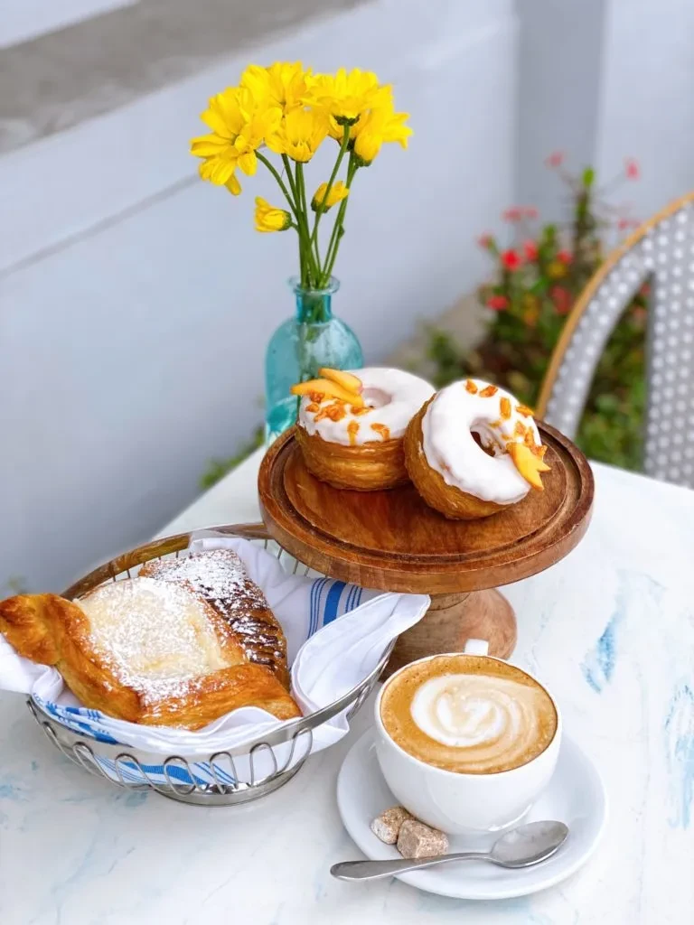 Outdoor brunch with coffee, a sugar-dusted pastry, and two cronuts.