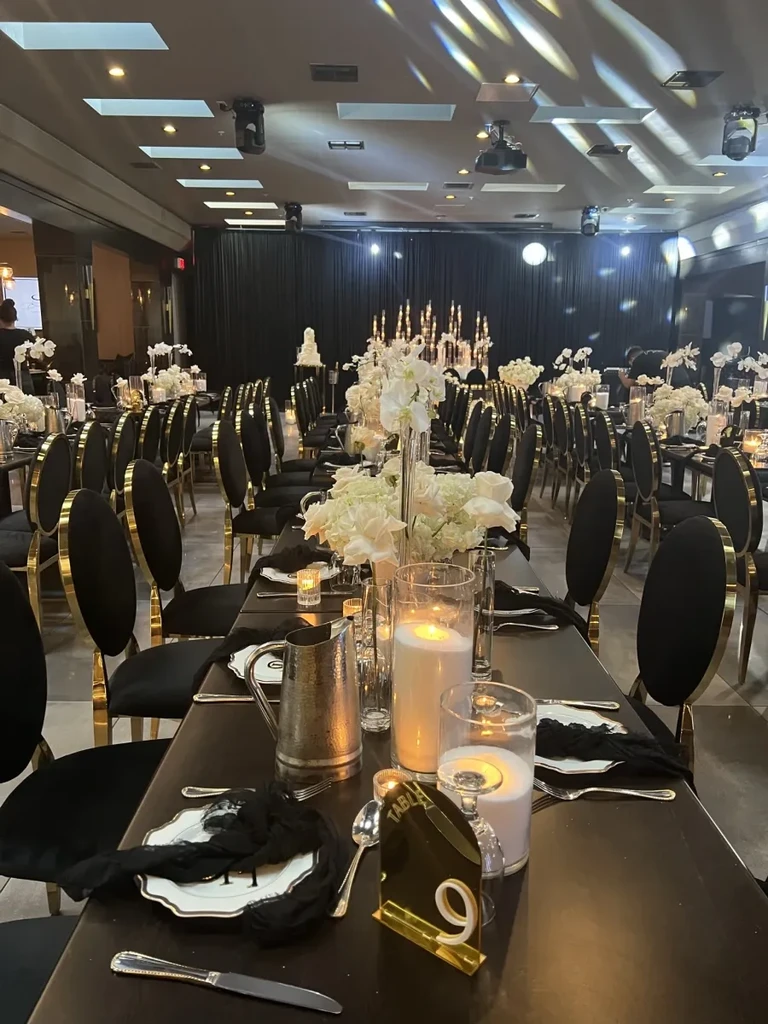 Elegant banquet hall with meticulously set black tables and a multi-tiered cake.
