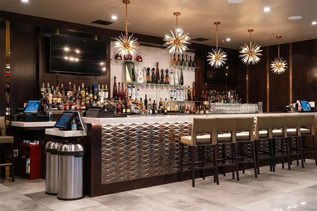 Modern bar with bronze counter, liquor display, and starburst chandeliers.