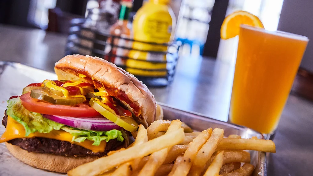 Classic cheeseburger, fries, and orange drink on a metal tray.