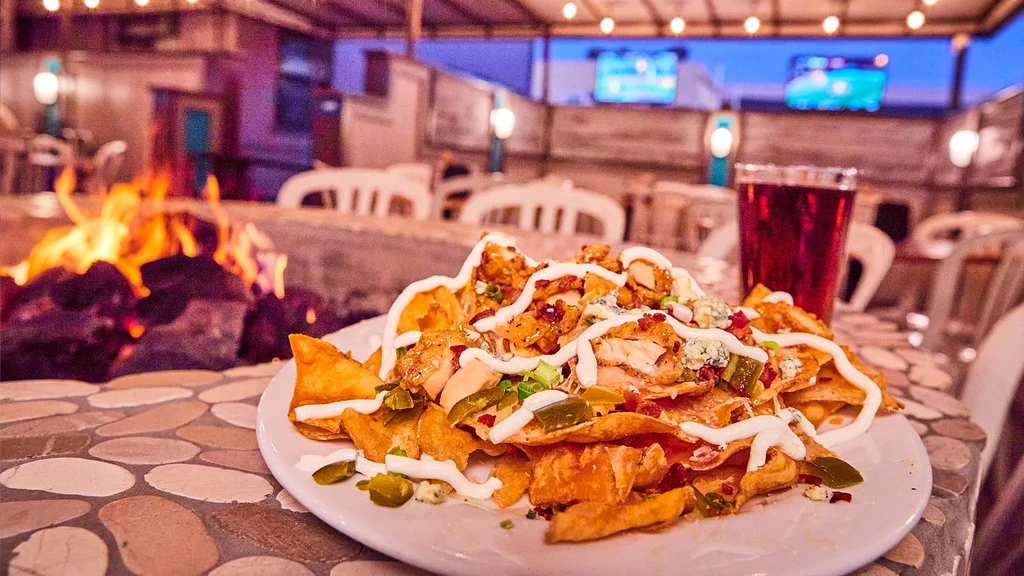 Close-up of chicken nachos with jalapeños on a lively outdoor patio.