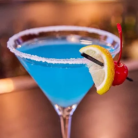 Blue martini cocktail with a sugared rim, lemon wedge, and cherry.