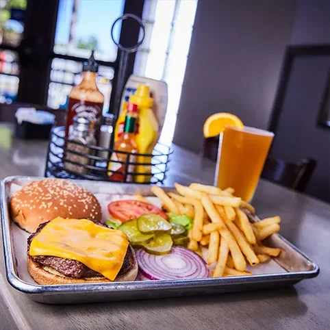 Cheeseburger and french fries on a metal tray with a beverage.