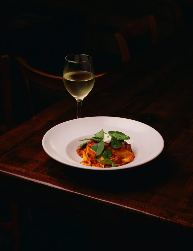 Broad pasta with red sauce, green garnish, creamy dollop, white wine.