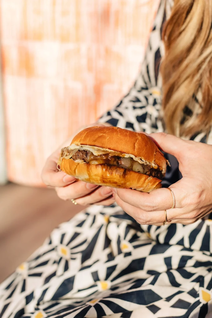 Ringed hands hold a gourmet burger with brioche bun and melted cheese.