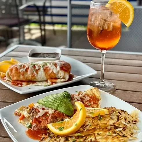 Omelet, burrito, and orange drink on an outdoor patio table.