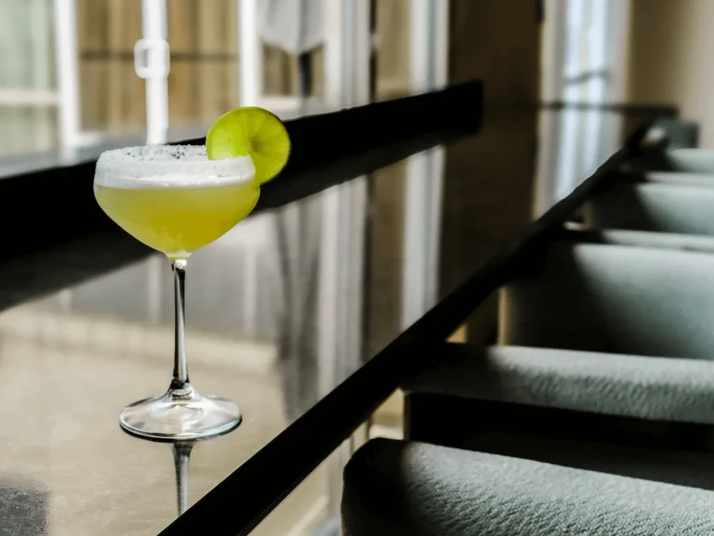 Pale cocktail with frothy top and lime in a coupe glass.