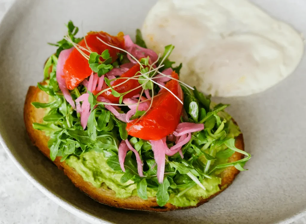 Avocado toast with arugula, tomatoes, pickled onions, and poached eggs.