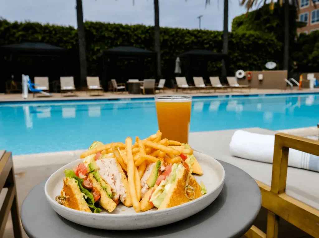 Club sandwich, golden fries, and orange drink beside a blue pool.