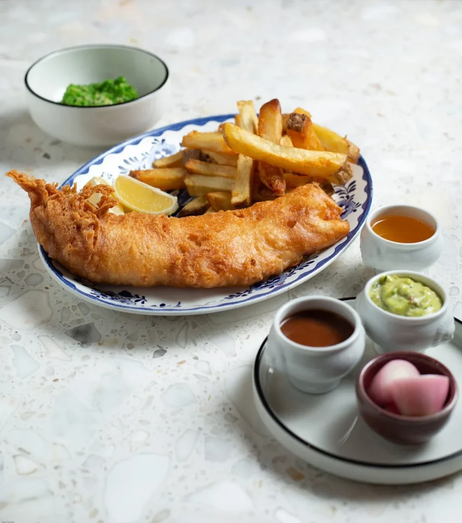 Classic fish and chips meal with mushy peas and various sauces.