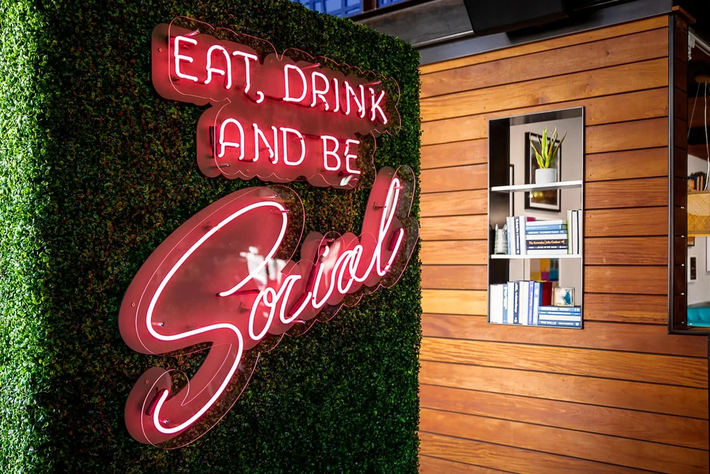 Red neon "EAT, DRINK AND BE Social" sign on a green wall.