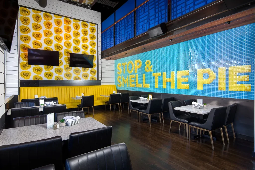 Restaurant interior with yellow booth and "STOP & SMELL THE PIE" mosaic wall.