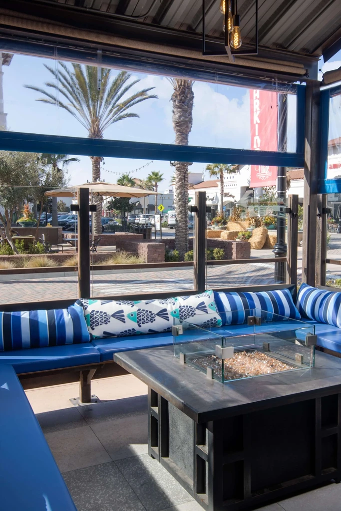 Outdoor seating: blue banquette, fire pit table, palm trees, clear sky.