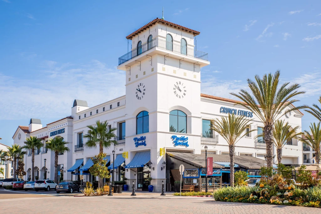Sunny Mediterranean complex, clock tower, palm trees, businesses, and pumpkins.