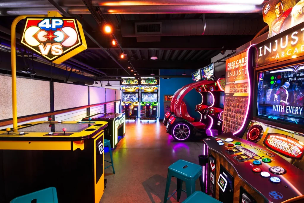 Brightly lit arcade interior featuring multiple racing, fighting, and multiplayer games.