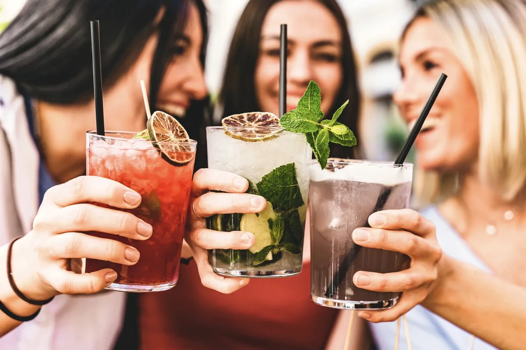 Close-up: Three colorful cocktails with garnishes, held by people toasting.