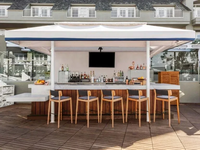 Outdoor bar with white canopy, wooden counter, and six bar stools.