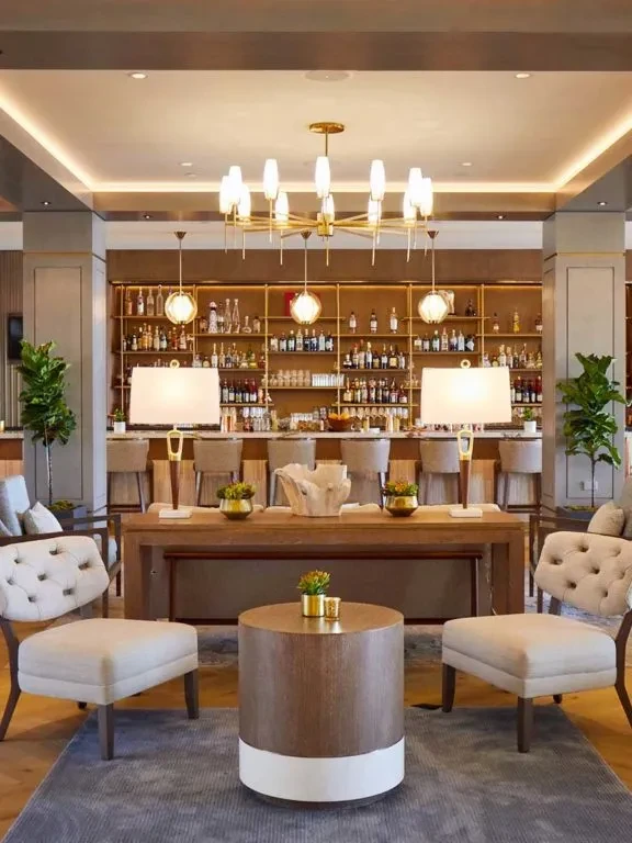 Modern bar and lounge, tufted armchairs, illuminated bar, and gold chandelier.