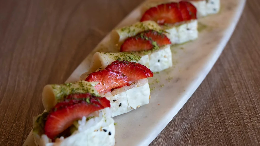 Six white dessert rolls with strawberries and green powder on marble.