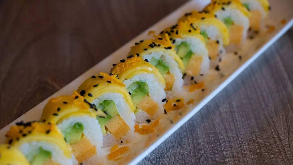 Seven sushi rolls with yellow wrap, green filling, and black sesame seeds.