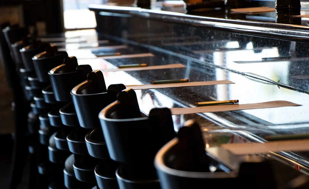 Dark, reflective bar with high-backed stools, paper, and pencils.