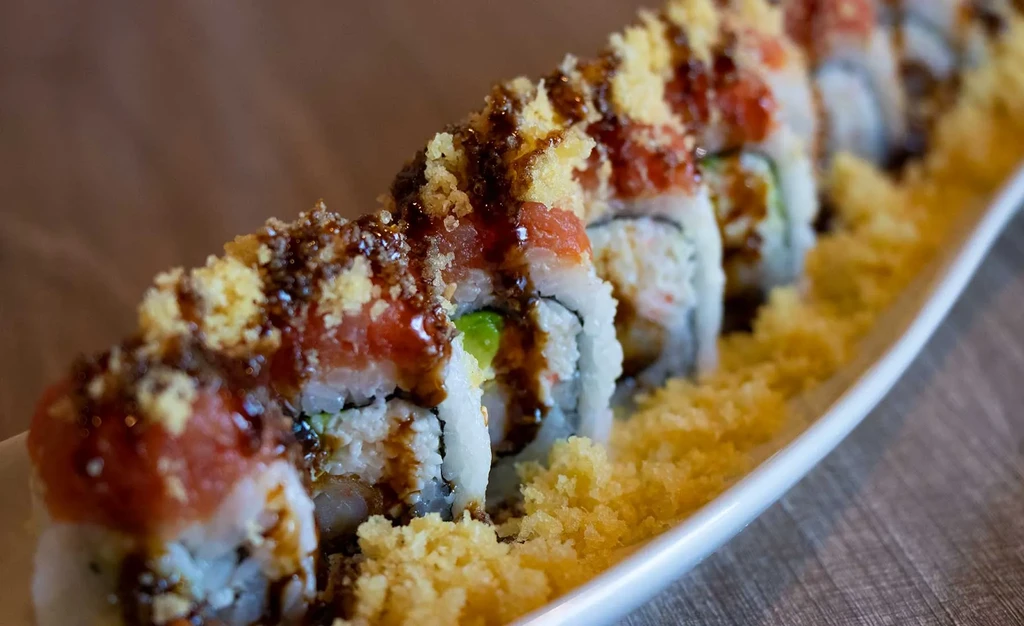 Sushi rolls topped with reddish-orange fish and golden tempura flakes.