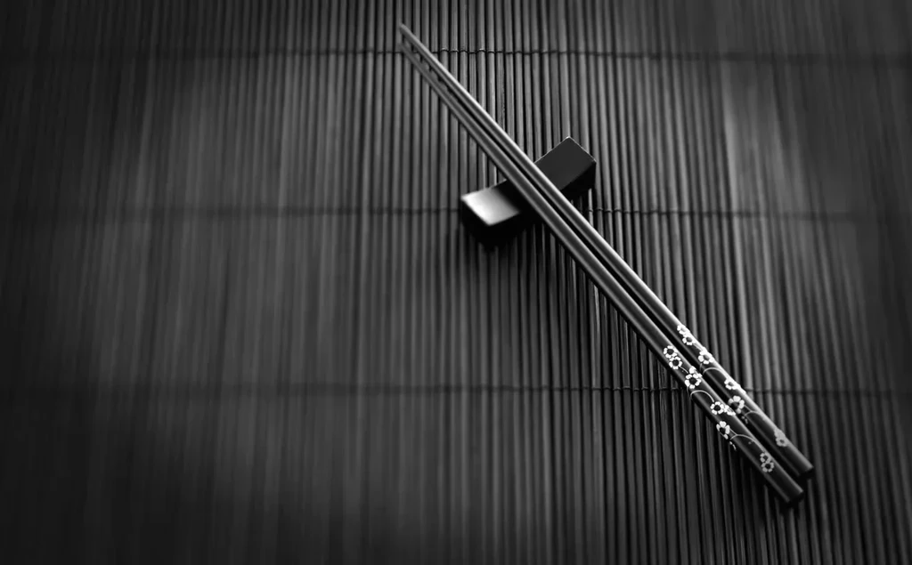 Black and white photo of patterned chopsticks on holder and mat.