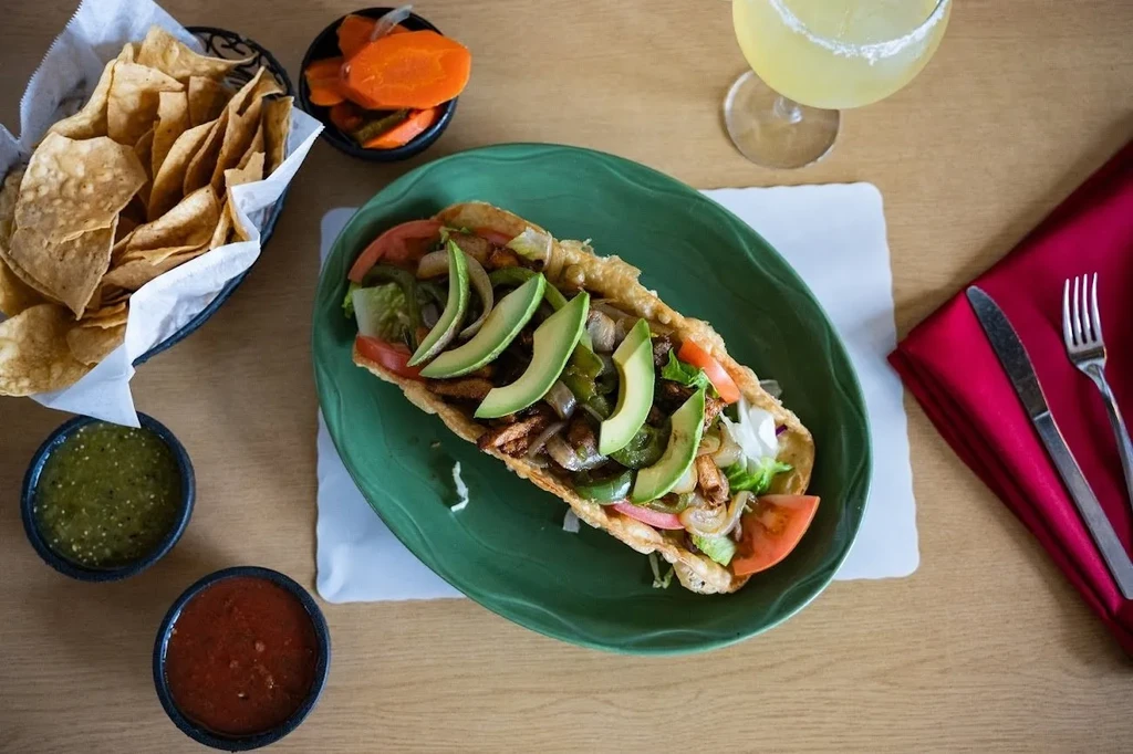 Top-down: colorful taco meal with chips, salsas, and margarita.