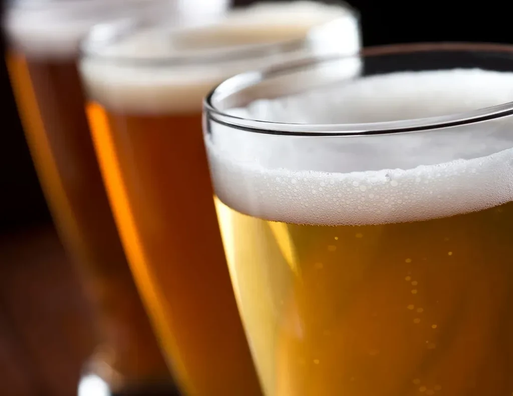 Three golden-amber beers with frothy heads, diagonally receding, one in focus.