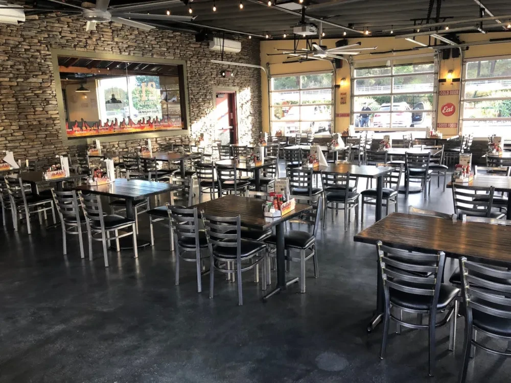 Empty restaurant dining area, stone wall, dark tables, polished floor, large windows.
