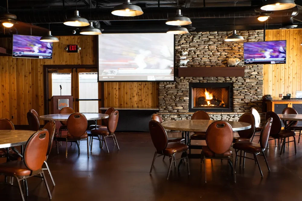 Empty rustic pub with tables, a fireplace, and multiple sports screens.