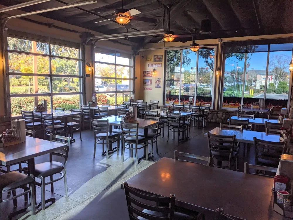 Empty restaurant dining area with many tables and large industrial windows.