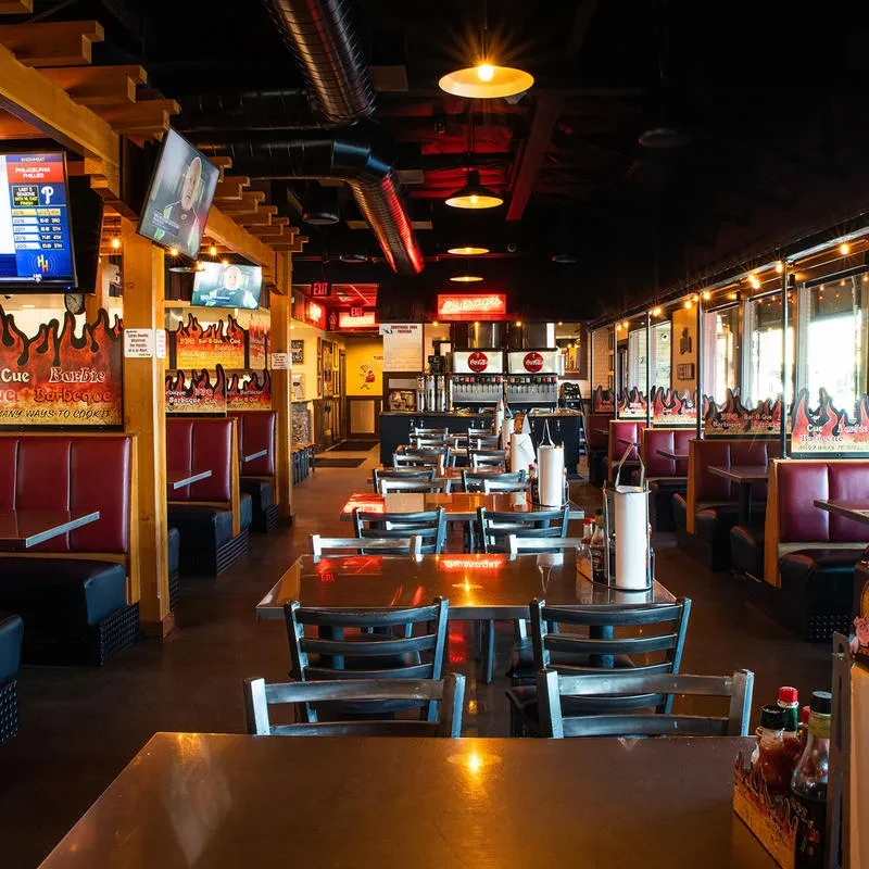 Empty casual restaurant interior with red booths, rustic industrial decor, and sports TVs.