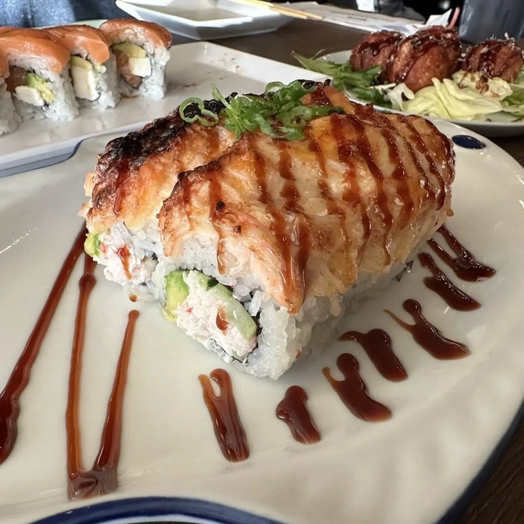Close-up of a seared salmon sushi roll and other Japanese dishes.