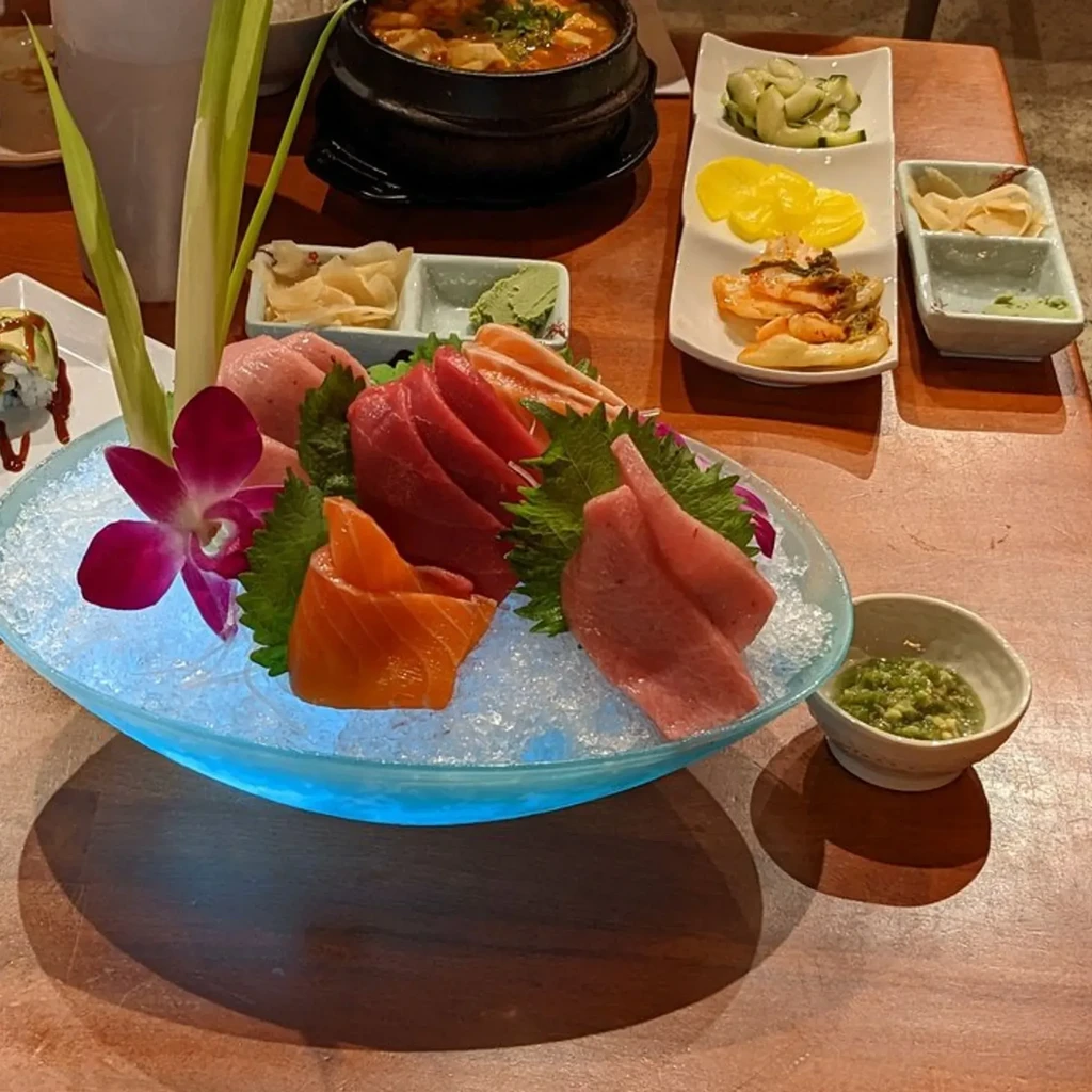Vibrant Asian meal: glowing sashimi, bubbling stew, sushi, and side dishes.