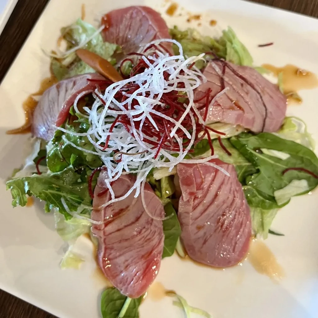 Plated thinly sliced pink meat on greens with radish and sauce.