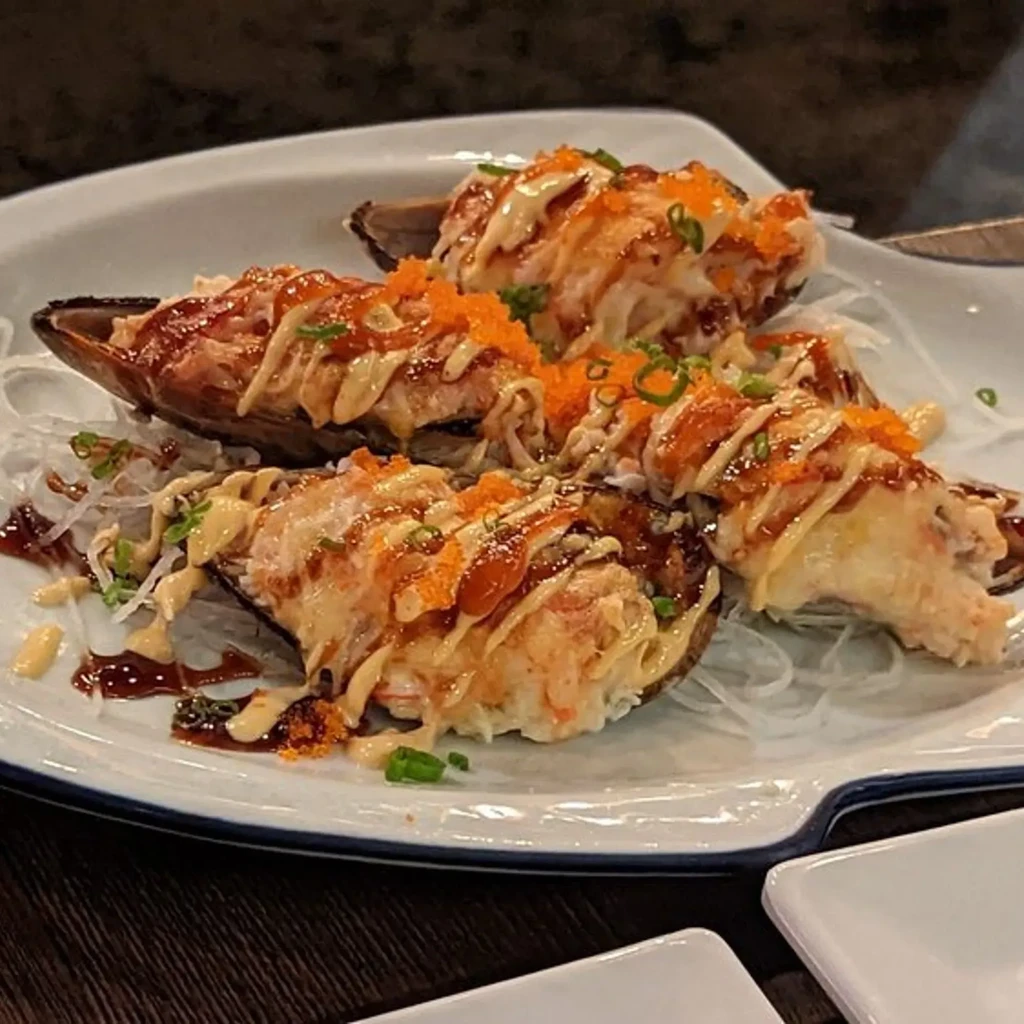 Baked mussels topped with creamy crab salad, savory sauces, tobiko, and onions.