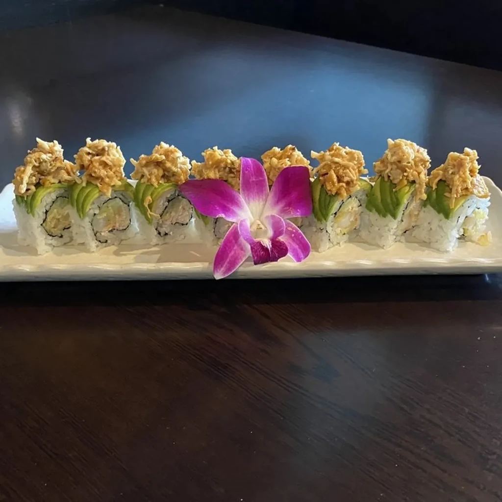 Platter of sushi rolls with avocado, seasoned topping, and a purple orchid.