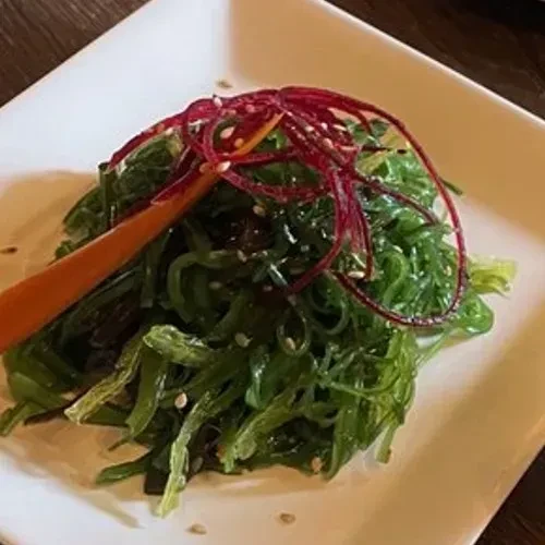 Vibrant green seaweed salad garnished with red strips, orange stick, sesame.