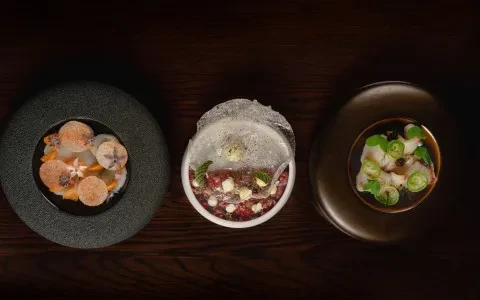Three elaborately plated dishes on a dark wooden table, overhead view.