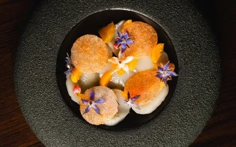 Intricately plated dish with pale rounds, orange wafers, and edible flowers.