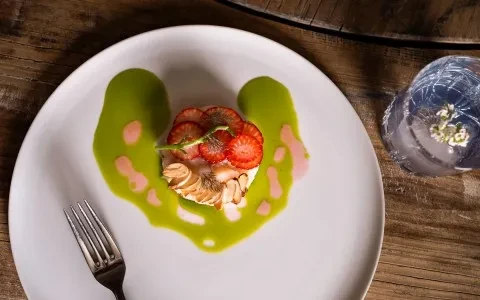 Plated dessert with strawberries, almonds, and green sauce on a wooden table.
